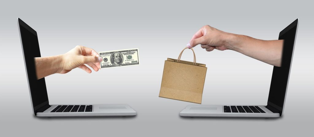An image depicting a hand emerging from a laptop, offering money to another hand emerging from another laptop, which is holding a bag, symbolizing digital financial transactions and online commerce in a visually metaphorical manner.